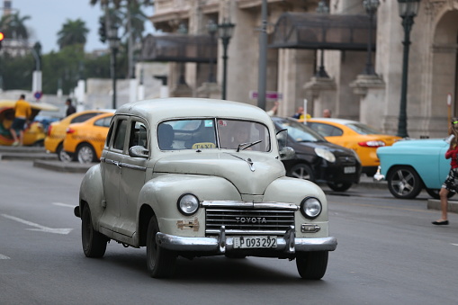 Havana, Cuba- 1/28/2017: Vintage cars are driving on the street. Incidental people on the background.