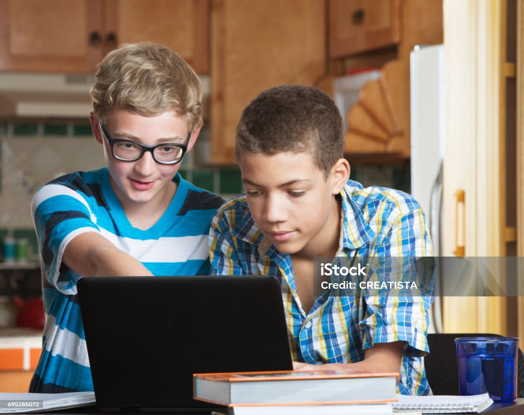 Teen friends doing homework Two male teen friends in kitchen with books and laptop Teenager Stock Photo