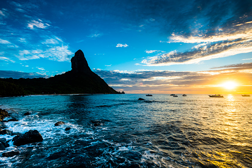 View of the sunset at 'Praia da Conceição' beach, facing the 'Morro do Pico', boats and nature in the archipelago of Fernando De Noronha - Brazil