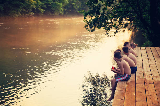A small group of children sitting by the river on the wooden deck, eating watermelon