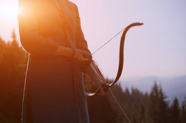 Traditional archery set – bows, quivers and feathered arrows – leaning against a wooden hut with a stone wall. An atmospheric scene with elements of historical reenactment or a medieval camp, perfect for illustrating themes related to archery, history and crafts.