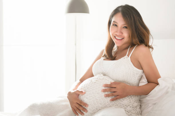 Beautiful pregnant woman touching her belly while lying on a bed at home stock photo