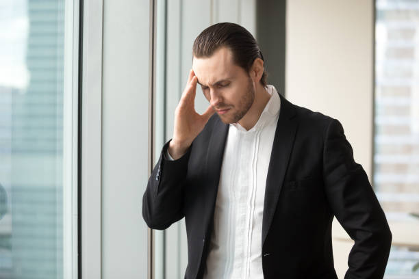 istock Man in formal wear standing with eyes closed touching temples 695358938