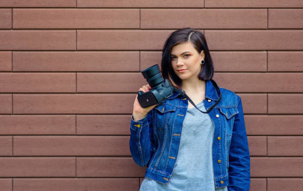 istock pretty girl with a blue jeans jacket holds a digital camera in her hands. 695371850