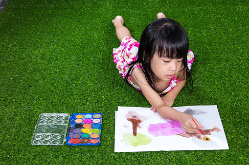 Asian Chinese little girl lying on the grass drawing and painting