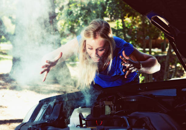 istock Blonde woman with smoking broken down car panics 695383650