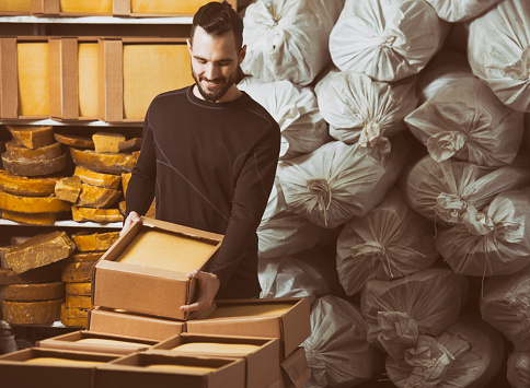 Factory man picking up a box with honeycomb wax sheets for shipping and delivery.