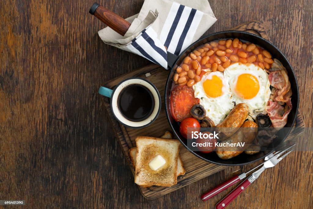 Full English breakfast with sausages, bacon, fried eggs, beans, toast and cup of coffee on wooden table with copy space Full English breakfast with sausages, bacon, fried eggs, beans, toast and cup of coffee on wooden table with copy space, top view English Breakfast Stock Photo