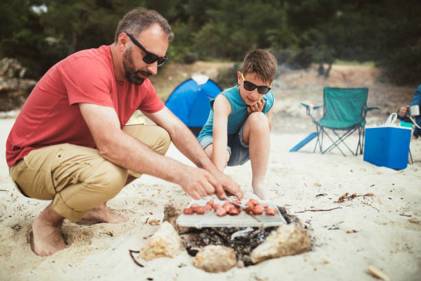 Together making a barbecue on a camping Photo of father and son making a barbecue on a camping on the beach. family bbq beach stock pictures, royalty-free photos & images