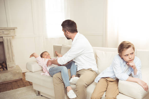 istock offended boy sitting on sofa while his father tickling daughter behind 695450936
