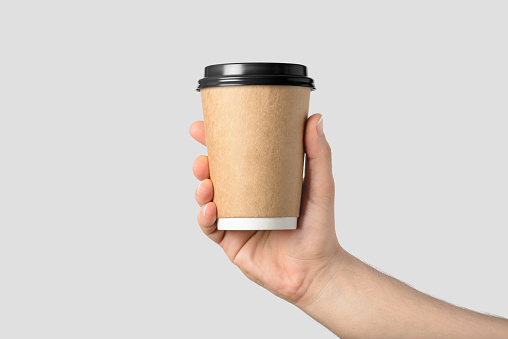 Mockup of male hand holding a Coffee paper cup isolated on light grey background.