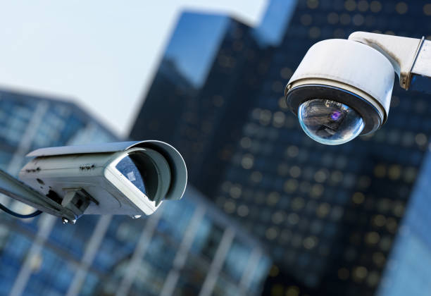 two cctv security camera in a city with blury business building on background - looking in camera imagens e fotografias de stock