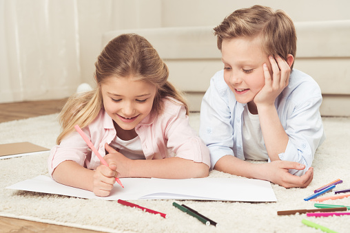 adorable pre-adolescent kids drawing pictures while lying on the floor at home