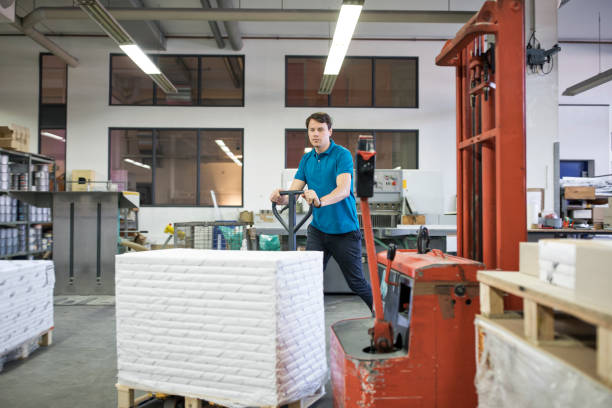 Worker pushing packages on hand pallet at factory Manual worker pushing stacked packages on hand pallet truck. Professional walking at printing plant warehouse with pallet jack. pallet jack handle stock pictures, royalty-free photos & images