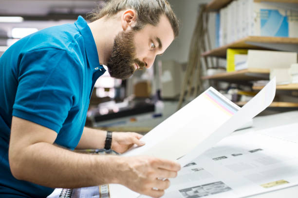 Designer working at printing industry Designer checking colour proofs on sample newspaper printout. Male worker working in printing factory. digital printing house stock pictures, royalty-free photos & images