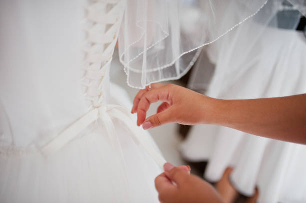 Bridesmaid helping a bride to tie a bow on a wedding dress.
