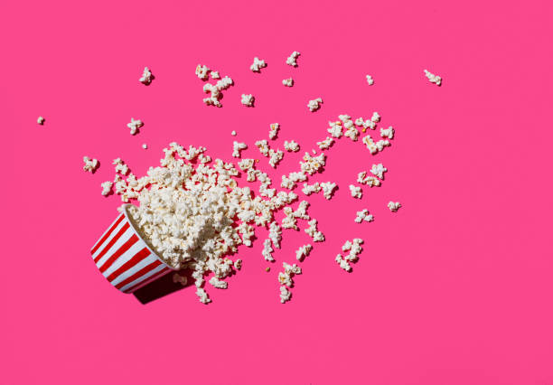 Spilled can of popcorn From above shot of striped can with popcorn spilled on pink surface. popcorn snack bowl isolated stock pictures, royalty-free photos & images