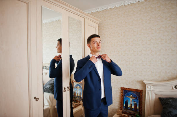 istock Handsome groom dressing up and getting ready for his wedding in the room. 695470050