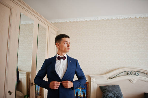 istock Handsome groom dressing up and getting ready for his wedding in the room. 695470128