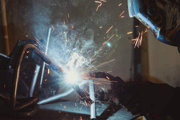 Worker with protective mask welding metal and producing smoke and sparks stock photo