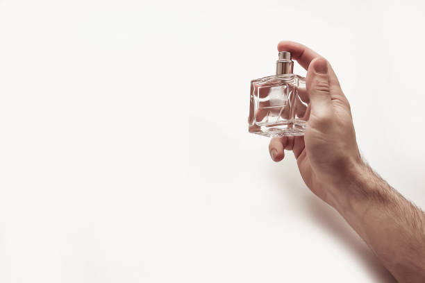 A man's hand holds a glass bottle with perfume on a light background