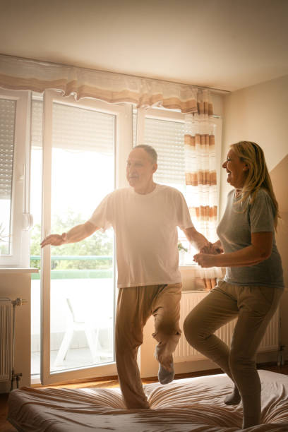 istock Senior couple dancing and jumping together on bed  holding hands. 695495332