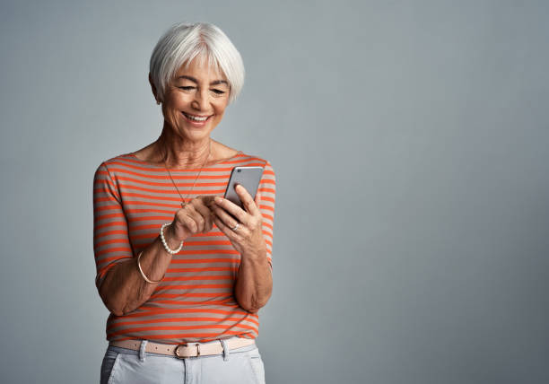 Connected to everyone and everything Shot of a senior woman using her cellphone against a grey background senior women stock pictures, royalty-free photos & images
