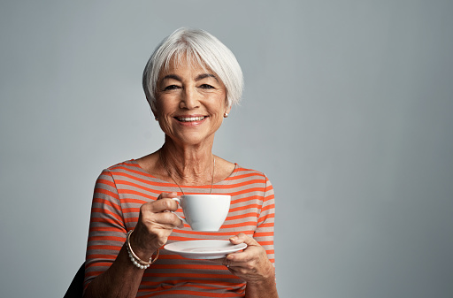 Shot of a senior woman enjoying a cup of coffee against a grey background