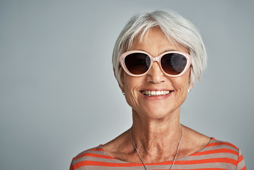 Studio shot of a senior woman wearing sunglasses against a grey background