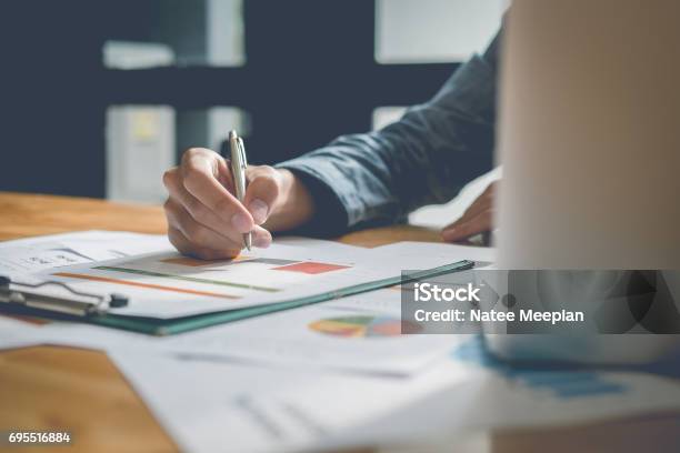 Businessman Analyzing Report On Chart With Laptop Computer In Office Stock Photo - Download Image Now