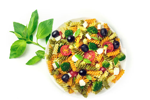 Plate of pasta salad with basil leaves on white