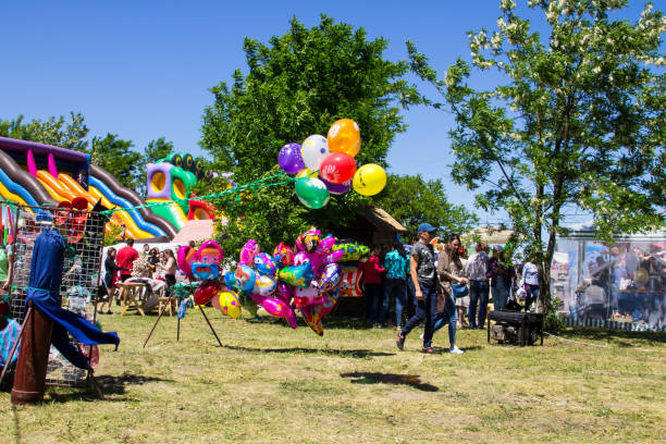 Color photo of a group of children trying to get balloons from a teenage girl.