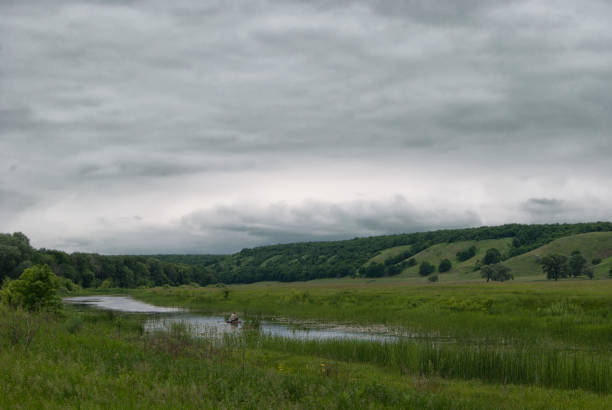istock Fisherman in a boat on a small lake in a cloudy hilly valley. 695559596