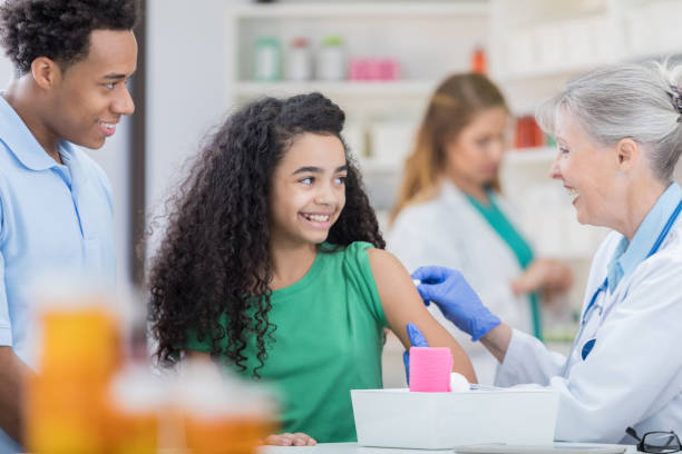 Cheerful girl prepares to receive back to school vaccines Healthcare professional rubs alcohol on tween girl's arm. The girl is preparing to receive back to school vaccines. injecting flu virus vaccination child stock pictures, royalty-free photos & images