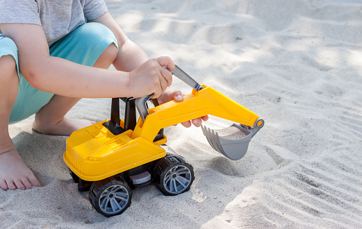 little boy playing with toy excavator in sand