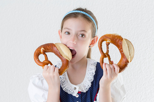 Bavarian little girl in traditional dress Dirndl biting into pretzel