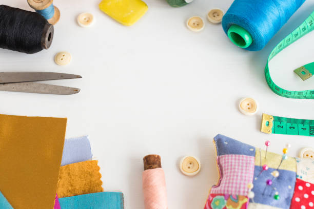 needlework, craft, sewing and tailoring concept - tools close-up on white desk, measuring meter, pink, blue and black thread spools, scraps of colorful fabric, pins and pincushion, white buttons, soap