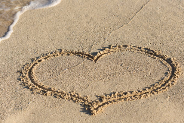 istock Shape of heart on sandy beach with wave's foam 695589020