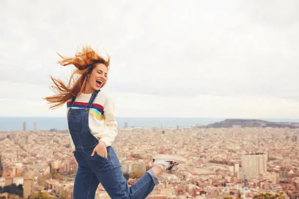 Cheerful woman dancing against cityscape. Happy female is wearing bib overalls. She is enjoying vacations.