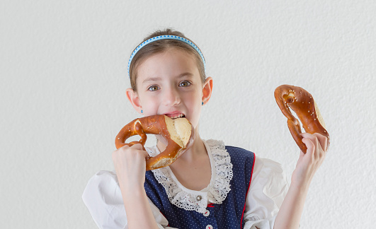 Bavarian little girl in traditional dress Dirndl biting into pretzel