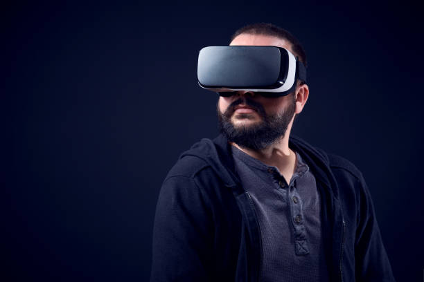 Young hipster bearded man wearing virtual reality goggles. Black background studio VR concept.