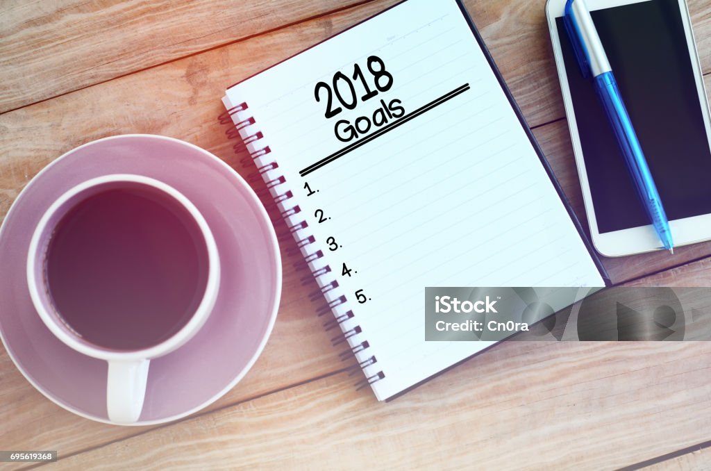 New Year's Goals 2018 goals list on note pad, wood table with coffee, pen and smart phone retro styled. 2018 Stock Photo