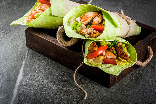 Mexican food. Healthy eating. Wrap sandwich: green lavash tortillas with spinach, fried chicken, fresh greens salad, tomatoes, yoghurt sauce. Wooden tray, dark stone table. Copy space