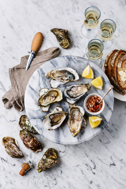 Open Oysters with lemon, bread, butter and champagne Open shucked Oysters with lemon, bread, butter and champagne on white marble background oyster stock pictures, royalty-free photos & images