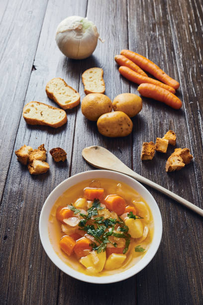 zuppa di verdure in ciotola bianca circondata da ingredienti su tavolo di legno - stuffing celery onion spoon foto e immagini stock