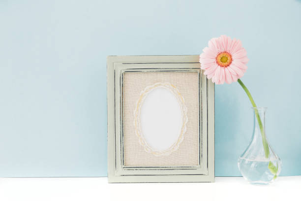 istock Empty wooden frame and flowers in vase on table on blue background. mock up 695641006