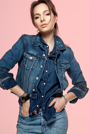 Portrait of a fashionable young woman in a denim jacket, jeans and a denim shirt on a pink background