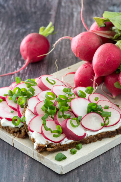 sandwich with radish, cheese and chives on wooden cutting board and dark background