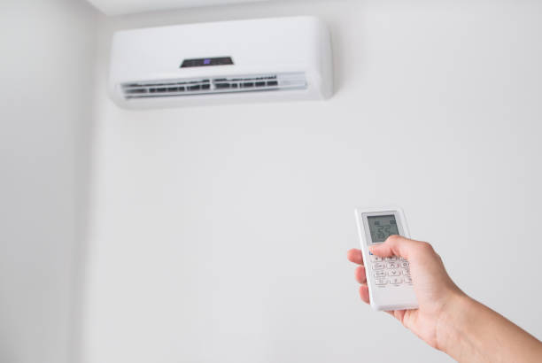 istock Hand holding remote control for air conditioner on white wall. 695678236