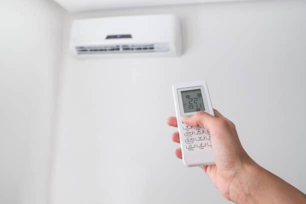 istock Hand holding remote control for air conditioner on white wall. 695678272